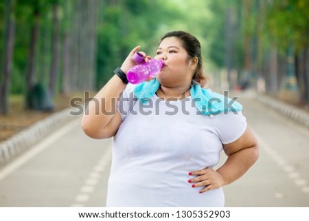 Picture of obese woman drinking water after doing a workout while standing in the road