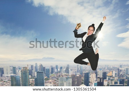 Portrait of excited businesswoman holding a trophy while dancing in the sky