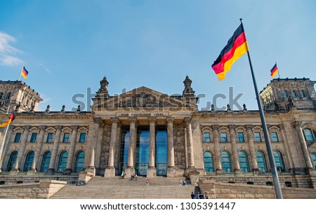 German flags waving in the wind at famous Reichstag building in berlin, seat of the German Parliament Deutscher Bundestag , on a sunny day with blue sky and clouds, central Berlin Mitte district,