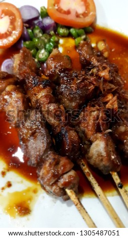 Close-up of "Sate Kambing" or mutton satay with soy sauce - Indonesian food, served with sliced ​​tomatoes, chili, and shallots.