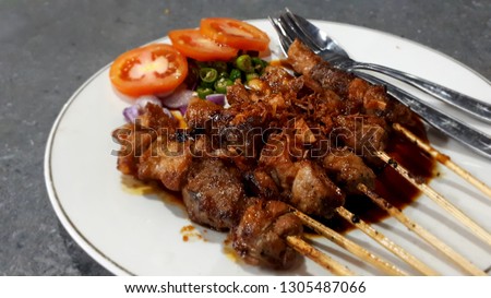 Close-up of "Sate Kambing" or mutton satay with soy sauce - Indonesian food, served with sliced ​​tomatoes, chili, and shallots.