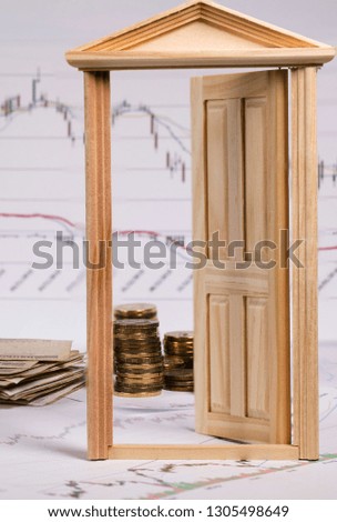 Coins on a stock market charts behind opened small wooden door. Closeup