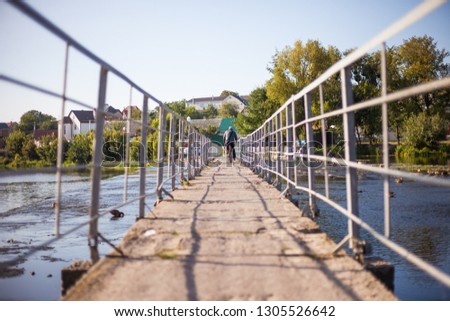 An elderly man rides an old bicycle across a river bridge.