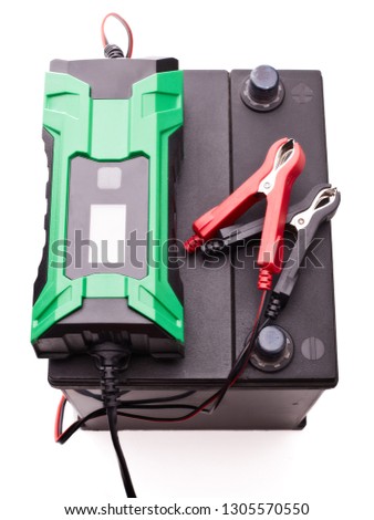 Black car accumulator battery and green charger  isolated on a white background. Top view. Acid battery,12 volts supply. Concept of service, maintenance, charging car battery, diy