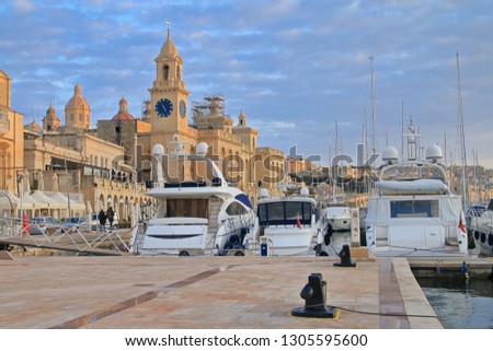 The photo was taken on the island of Malta in the city of Birgu. The picture shows yachts moored on the coast of the city in the evening against the backdrop of ancient architecture.