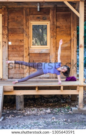 A woman practices yoga on the porch of an old wooden house. The girl goes in for sports in the yard on a warm spring day. Slender brunette doing asanas.