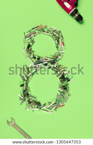 The conceptual composition from set of nails, screws and tools about Eight march womans day holiday on a green background. The number 8 in decor. Top view. The women in male occupations