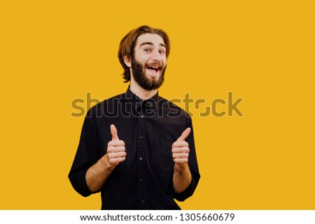  portrait of a beautiful Caucasian young man with a beard shows his thumb up, laughs with joy, has a pleasant smile, dark hair,  Happiness and the concept of trust,