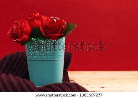 beautiful roses flowers in plastic vase with purple winter scarf on wood table with red background