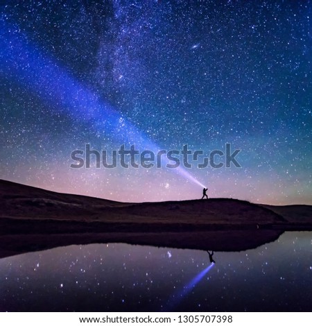 Man with flashlight and bright night sky. Amazing shot with stars and Milky Way reflecting in water