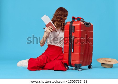 pretty woman next to a red suitcase on a blue isolated travel background