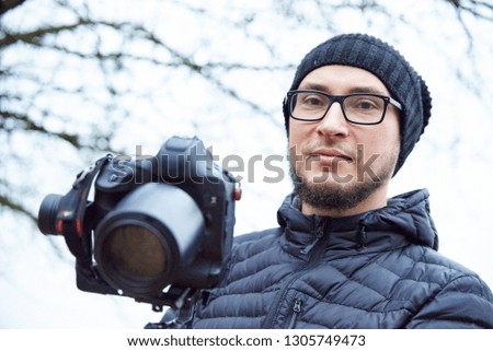 male photographer in a cap shoots a video camera on a cold outside photo.