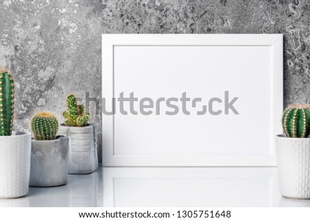 Empty white frame on a gray stone wall background. Mockup. White shelf. Cactuses in concrete pots as interior decoration