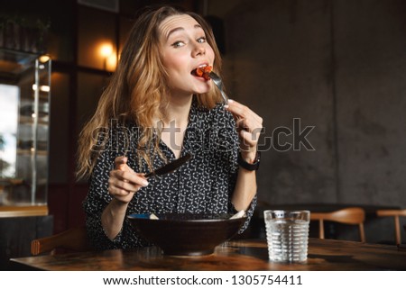 Photo of excited beautiful young pretty woman sitting in cafe indoors have a breakfast.