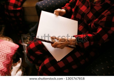 Christmas picture of an old lady holding the album with her photos. In a family circle near the christmas tree and her children. Checkered red pajama and comfortable cozy clothes. Warm atmosphere.