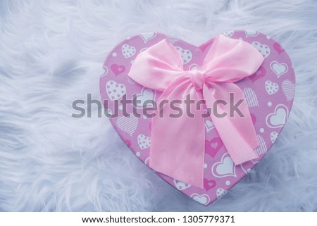 Pink box in the shape of a heart with a pink bow on a white fur rug.