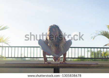 Young woman practicing yoga, advanced yoga outside. 
Yoga on the roof at dawn overlooking the palm trees and rice fields of Bali.