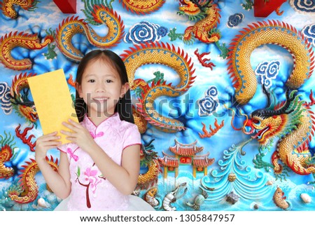 Happy little Asian child girl wearing pink traditional cheongsam dress smiling while receiving gold envelope packet on chinese dragon wall background. Happy chinese new year concept.