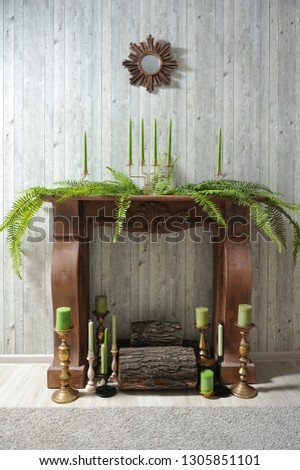 Brown wooden fireplace with green candles and candlesticks in gold and copper on the background of wallpaper under the texture of wood, as well as a fireplace decorated with leaves of fern