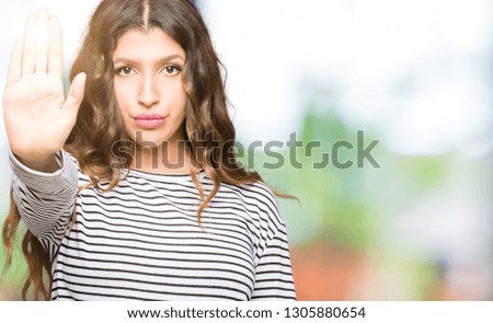 Young beautiful woman wearing stripes sweater doing stop sing with palm of the hand. Warning expression with negative and serious gesture on the face.
