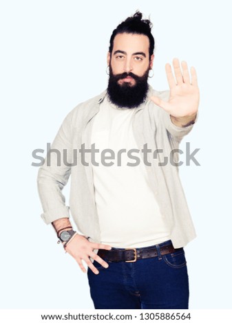 Young man with long hair, beard and earrings doing stop sing with palm of the hand. Warning expression with negative and serious gesture on the face.