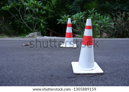 White and red plastic traffic cone striped on concrete road is damaged.