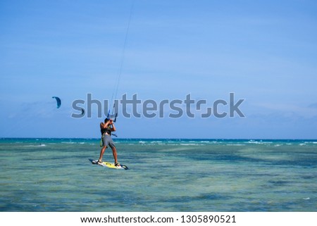 Kitesurfing, kiteboarding, kite surf. Extreme sport kitesurfing in tropical blue ocean, clear beach. Stock photo image of kitesurfing on the waves of the beautiful sea in Vietnam. Kite surfer