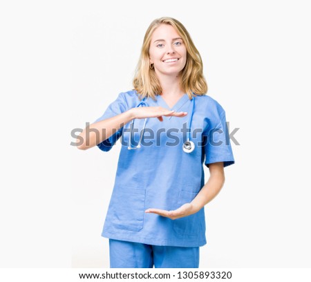 Beautiful young doctor woman wearing medical uniform over isolated background gesturing with hands showing big and large size sign, measure symbol. Smiling looking at the camera. Measuring concept.
