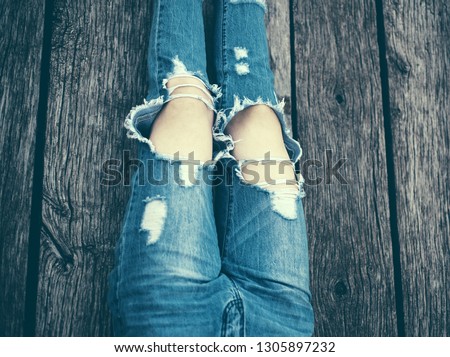 Ripped jeans female feet. Fashion woman's legs in jeans and shoes on wooden floor. Girl is sitting, wearing ripped jeans, hipster style, casual, clothes for youth, sporty style