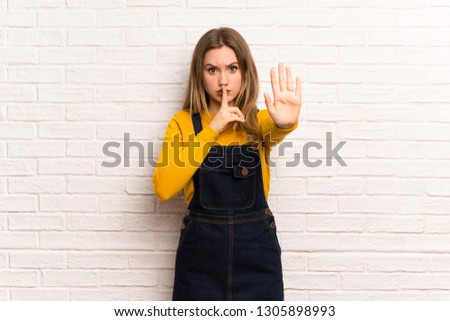 Teenager girl over white brick wall making stop gesture denying a situation that thinks wrong