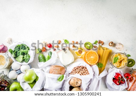 Zero waste shopping and sustanable lifestyle concept, various farm organic vegetables, grains, pasta, eggs and fruits in reusable packaging supermarket bags. copy space top view, white concrete table