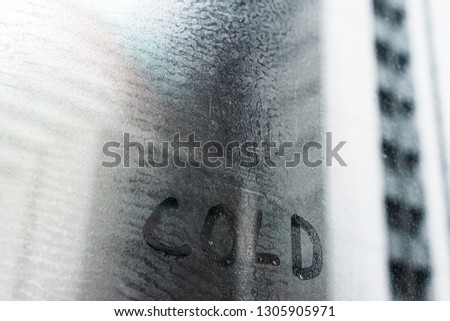 "Cold" word written on fresh condensation on window glass fogged textured natural background. Weather conditions concept. 