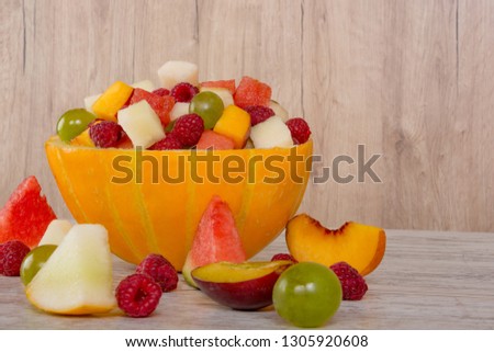 Fruit salad. Peach, watermelon, melon, raspberry, plum, grapes, diced lie in a melon salad bowl on a white wooden background. Pieces of fruit. Place for text.