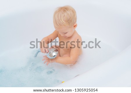Kid baby take a bath in white bathtub. Kid having bath. Happy baby face in bubble bath. Happy baby having a bath and playing with toys