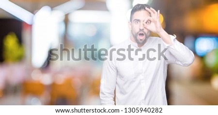 Young business man over isolated background doing ok gesture shocked with surprised face, eye looking through fingers. Unbelieving expression.