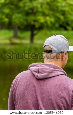 Photo of Millennial with Purple Hoodie and Grey Hat Spending Some Quality Leisure Time By the Lake on Countryside - Concept of Educated Generation Member, Free Space for Text