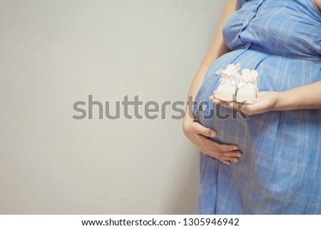 pregnant woman holds a pair of shoes or socks in her hand to prepare for her child.