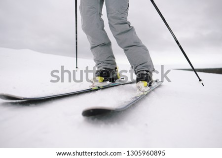 A beautiful young chewing woman in an extreme sports suit, hat and a helmet with a mask on a winter slope is skiing against the background of the forest. Alpine skiing and winter holidays.