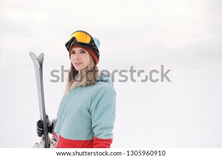A beautiful young chew in an extreme sports suit, a hat and a helmet with a mask on the winter slope is holding alpine skis. Alpine skiing and winter holidays.