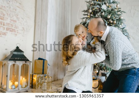 Christmas family portrait. Charming man, woman and their little son have fun posing before a Christmas tree in a bright room