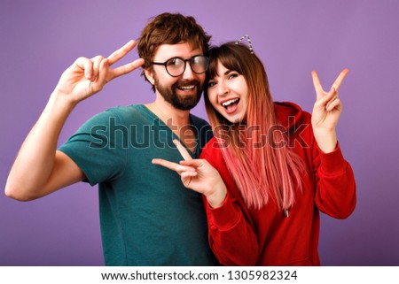 Positive studio portrait of crazy young hipster couple having fun together, showing peace gesture laughing and screaming, wearing stylish casual hoodie and T-shirt, family and friends picture.