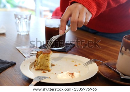 Close-up pictures of hands scooping banana cakes to eat with a fork. Coupled with drinking coffee on a wooden table in a coffee shop