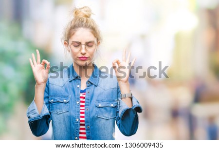 Young beautiful blonde woman wearing glasses over isolated background relax and smiling with eyes closed doing meditation gesture with fingers. Yoga concept.