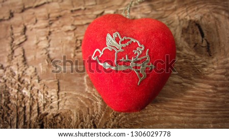 Pendant-2 is a bright red heart with the symbol of the Amur, which shoots the bow lays on a wooden background. 