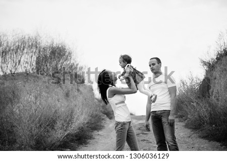 Happy young family in white t-shirts and blue jeans with a small daughter in dress hugging, outdoors background