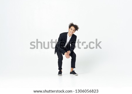 Cute elegant man in a dark suit crouches on a light background