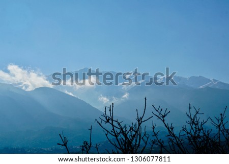 The White Mountains including Pakhnes in Crete, Greece during a sunny December day, the mountains are snow covered with some olive leaves in front of                         