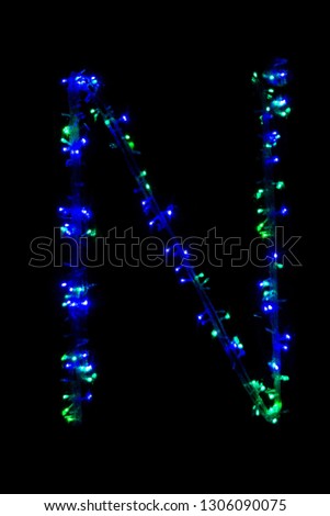 The letter "N" of the English alphabet made of blue electric garland on a dark background, blur, bokeh, isolated on black