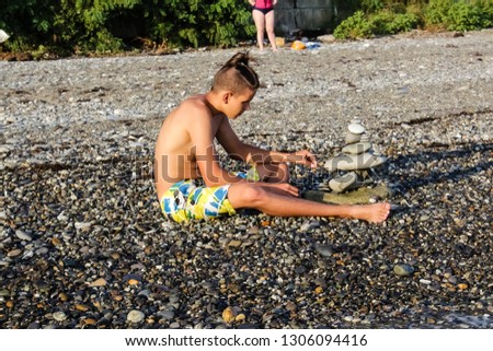 Young man builds a cairn on the sea beach.