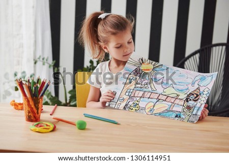 She will be professional painter one day. Cute little girl in art school shows her first picture drawn by pencils and markers.